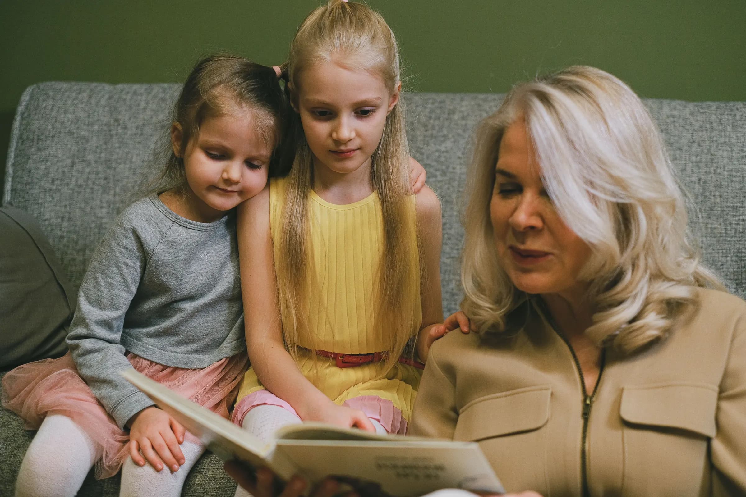Mamie lit un livre à ses deux petites-filles sur le canapé.